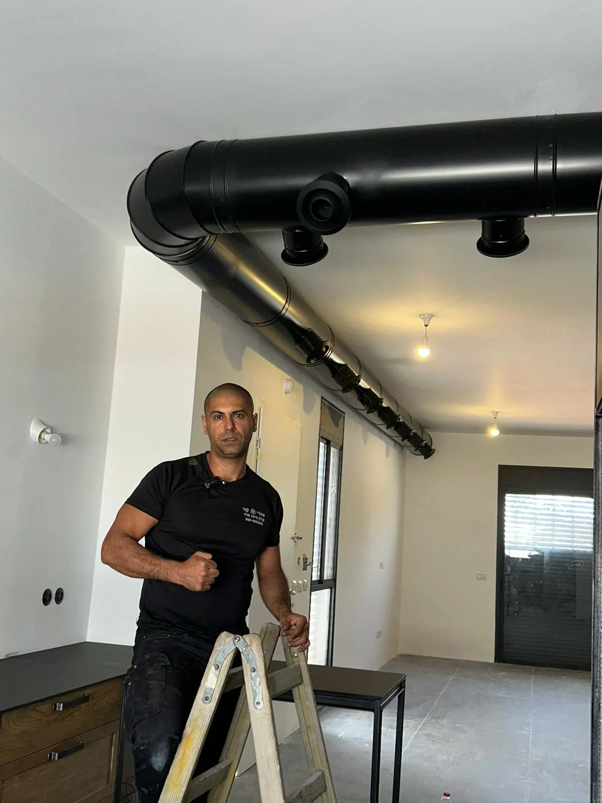 תעלת מיזוג עגולה שחורה חשופה עם מפזרים שחורים לאורך תקרת דירה בסגנון לופט