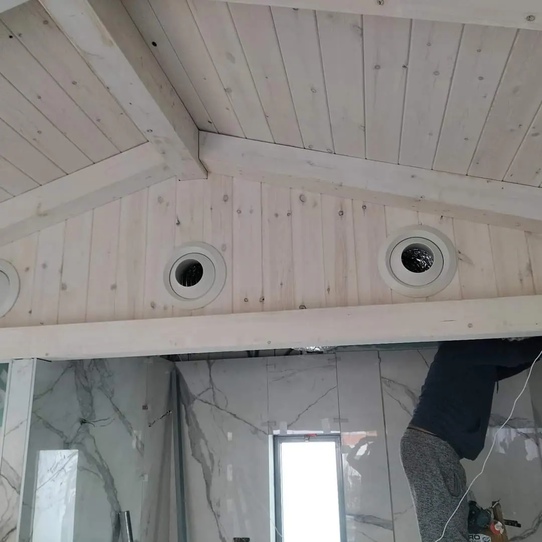 תקרת עץ משופעת מולבנת עם מפזרים עגולים לבנים מעל חדר רחצה מחופה שיש